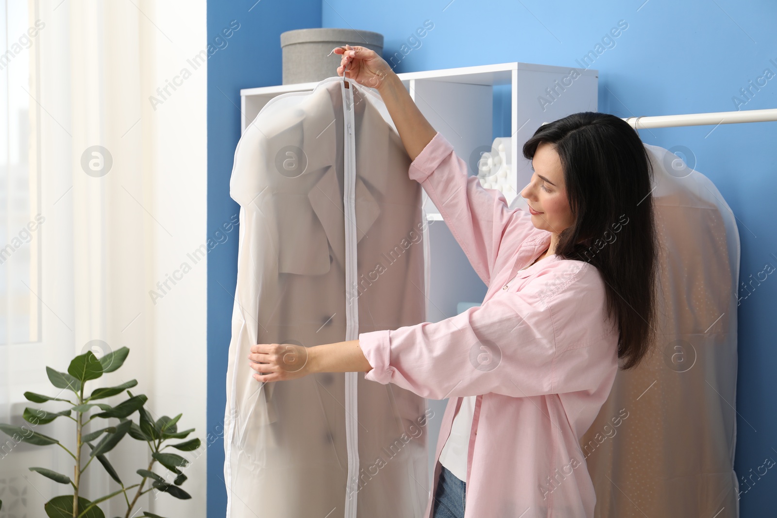 Photo of Woman holding garment cover with clothes indoors