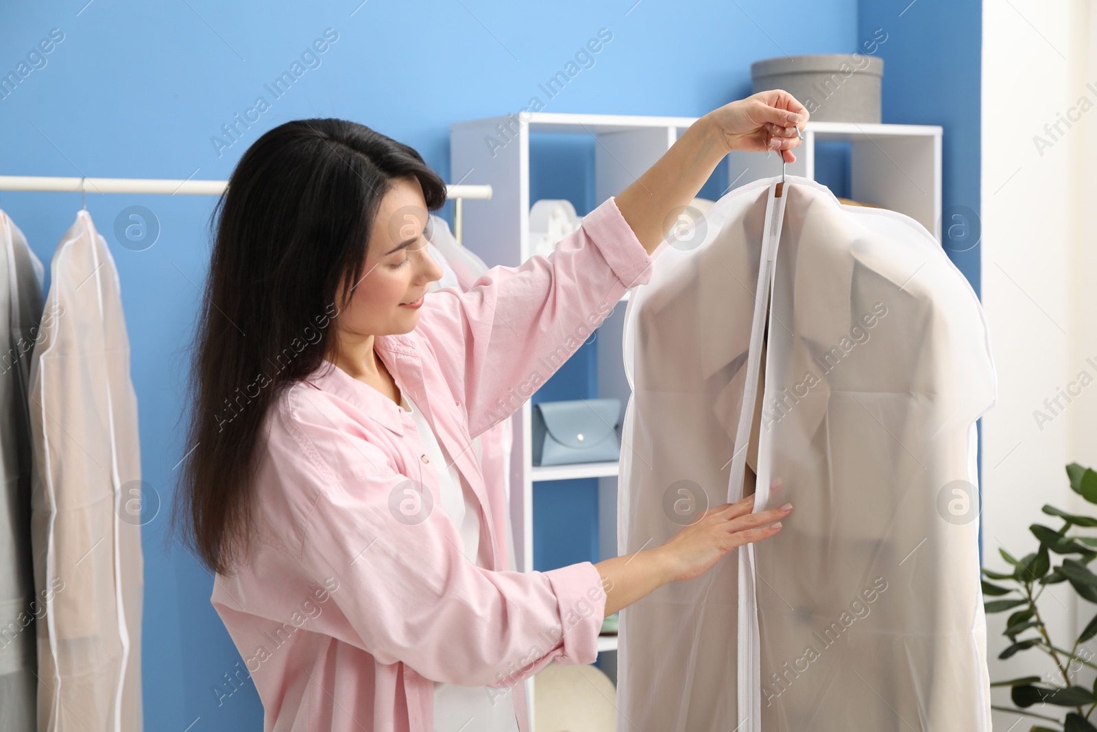 Photo of Woman holding garment cover with clothes indoors