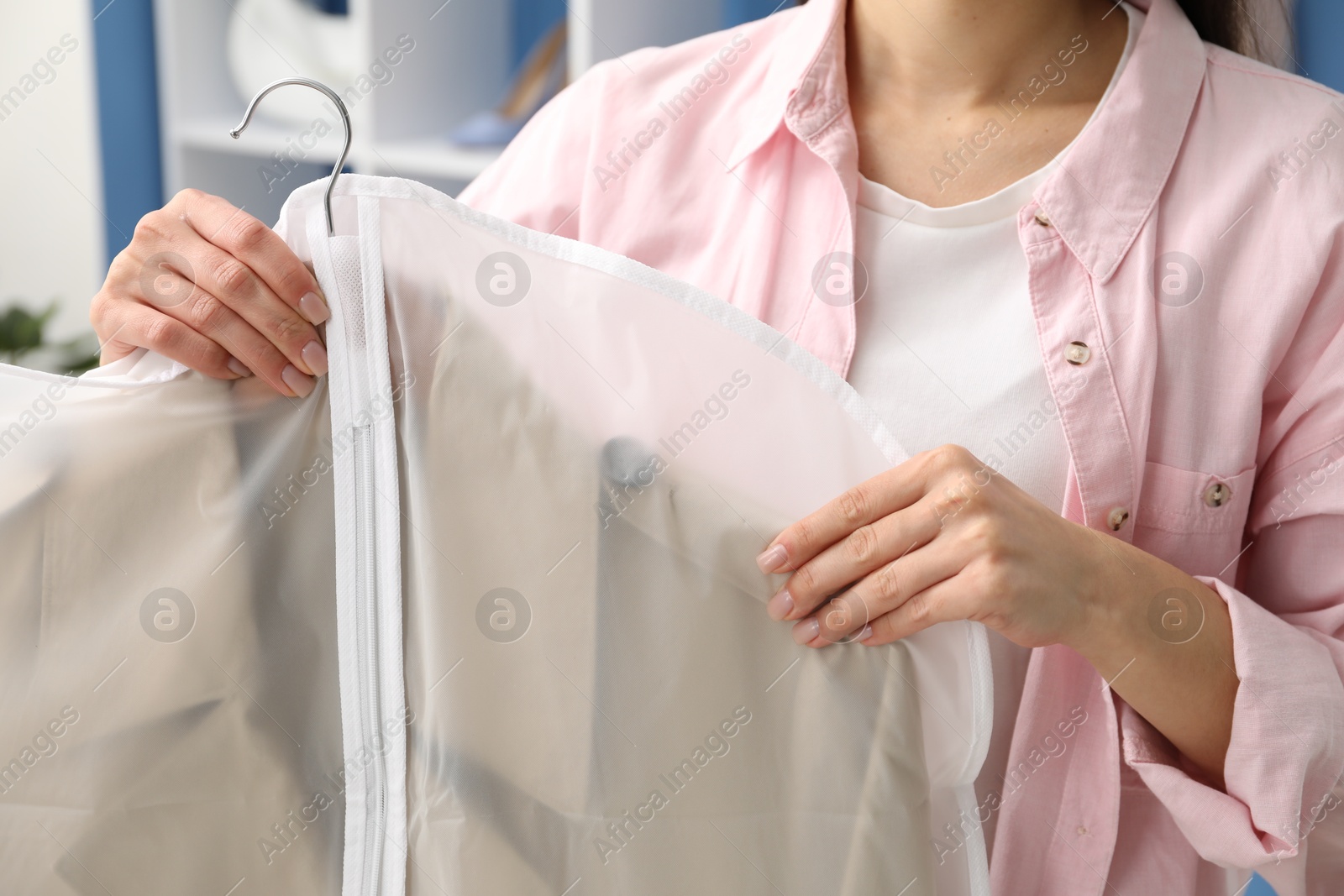 Photo of Woman holding garment cover with clothes indoors, closeup