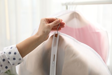 Photo of Woman holding garment cover with clothes indoors, closeup