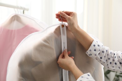 Photo of Woman zipping garment cover with clothes indoors, closeup