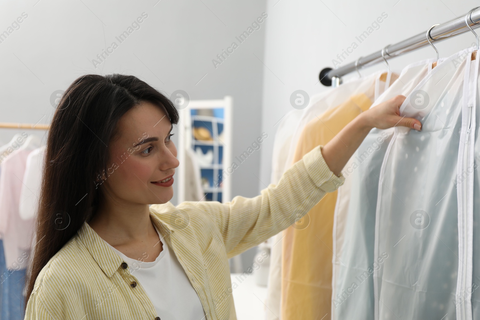 Photo of Woman taking garment cover with clothes from rack indoors