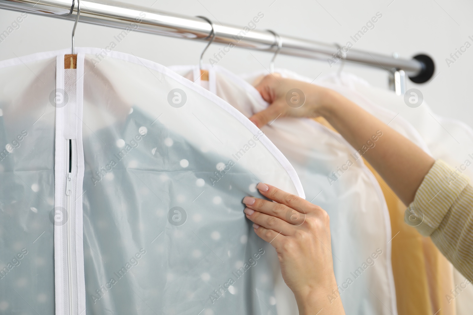 Photo of Woman taking garment cover with clothes from rack indoors, closeup