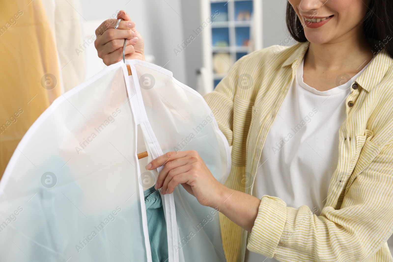 Photo of Woman holding garment cover with clothes indoors, closeup