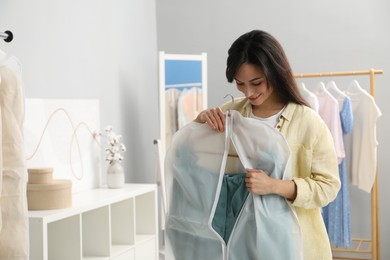 Woman holding garment cover with clothes indoors