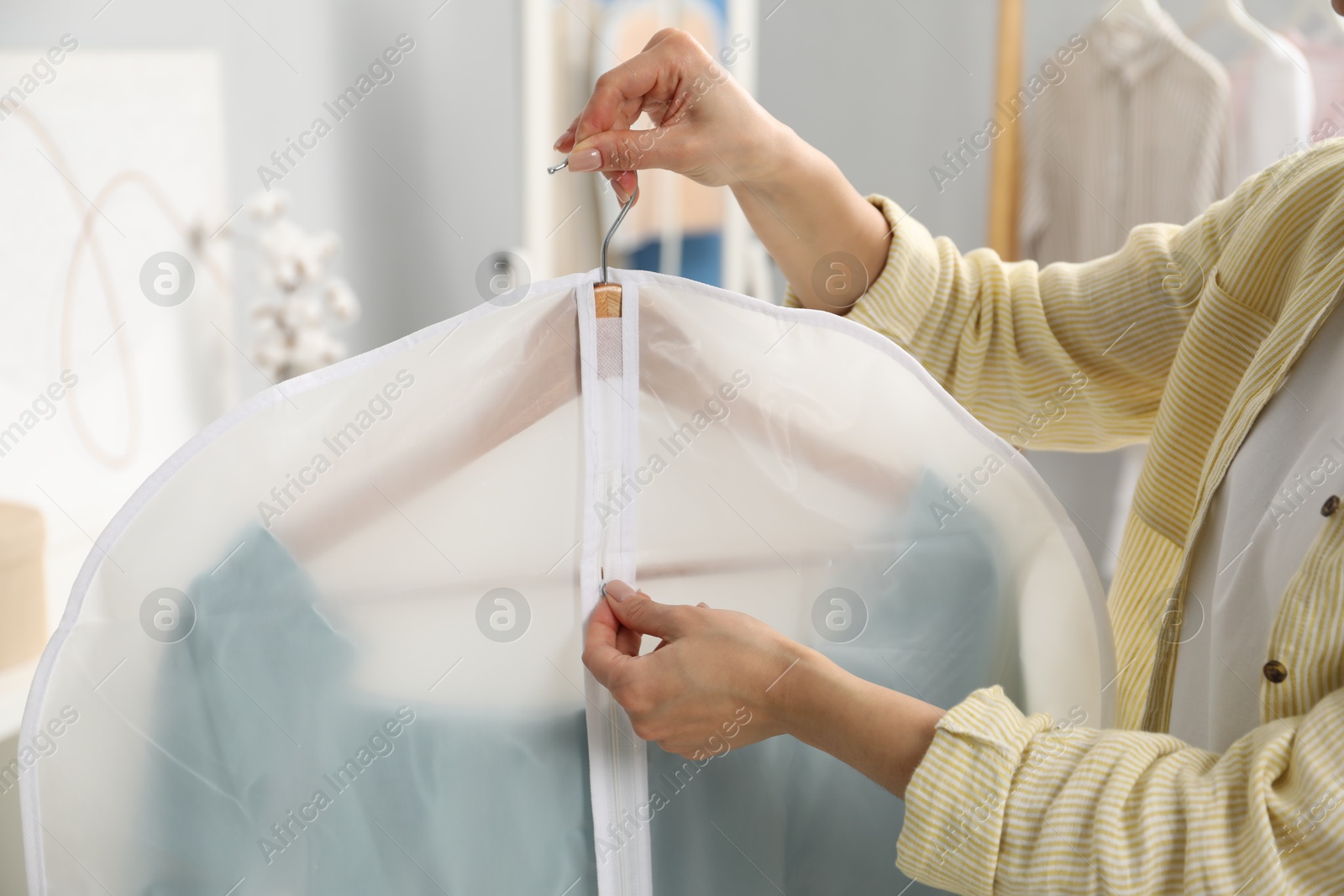 Photo of Woman zipping garment cover with clothes indoors, closeup