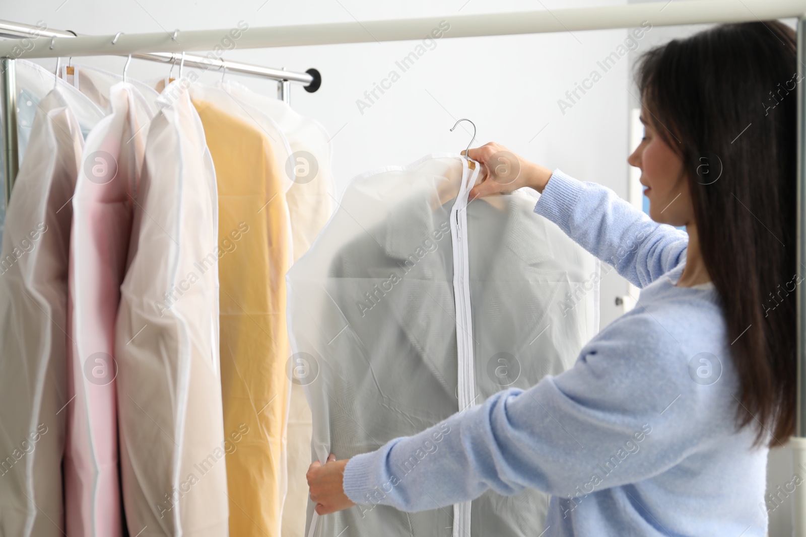 Photo of Woman holding garment cover with clothes indoors