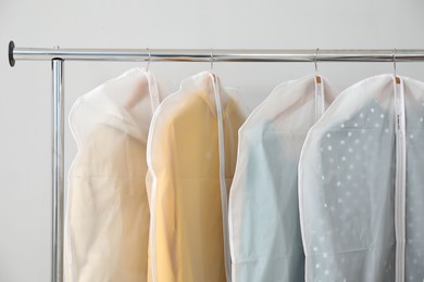 Photo of Garment covers with clothes on rack near white wall indoors, closeup