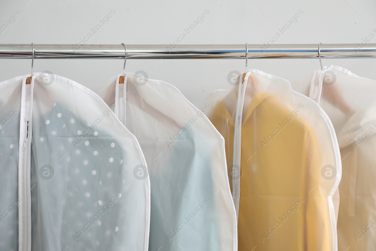 Photo of Garment covers with clothes on rack near white wall indoors, closeup