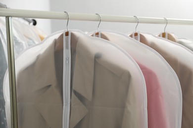 Photo of Garment covers with clothes on rack indoors, closeup