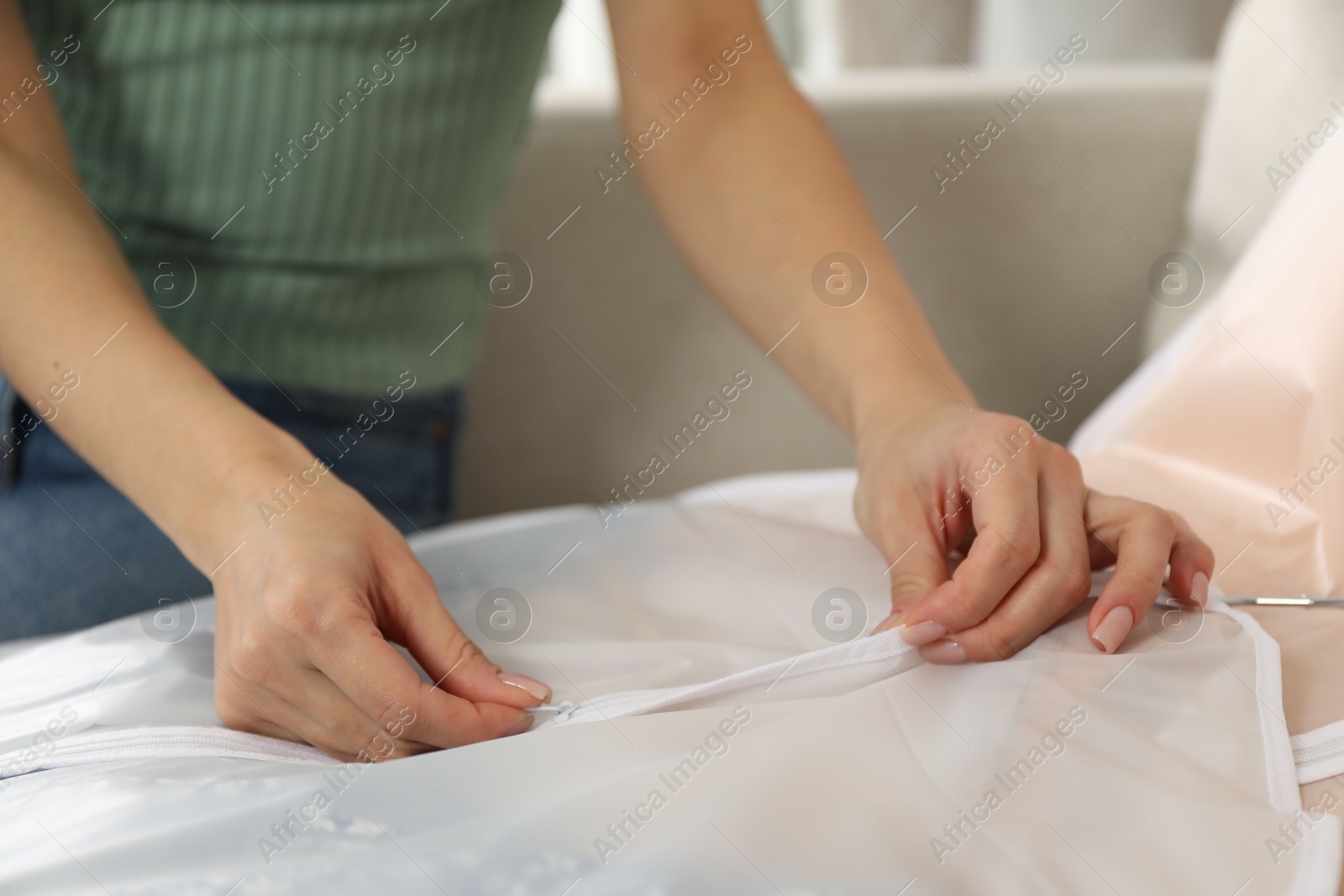 Photo of Woman zipping garment cover with clothes indoors, closeup