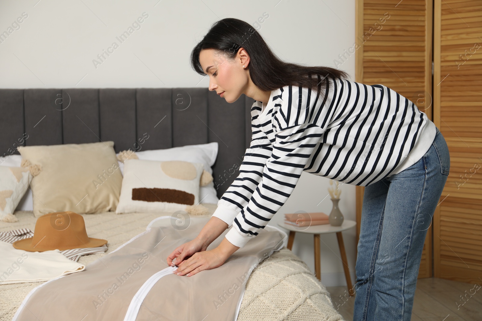 Photo of Woman putting clothes into garment cover indoors