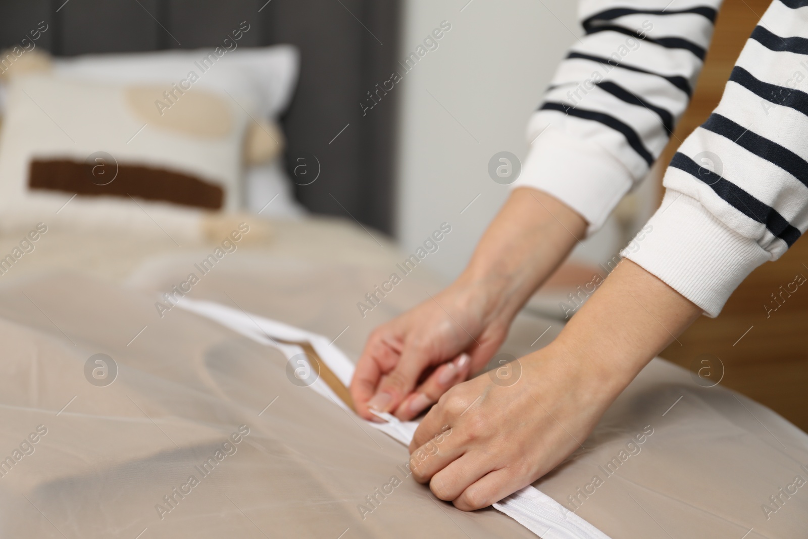 Photo of Woman zipping garment cover with clothes on bed indoors, closeup