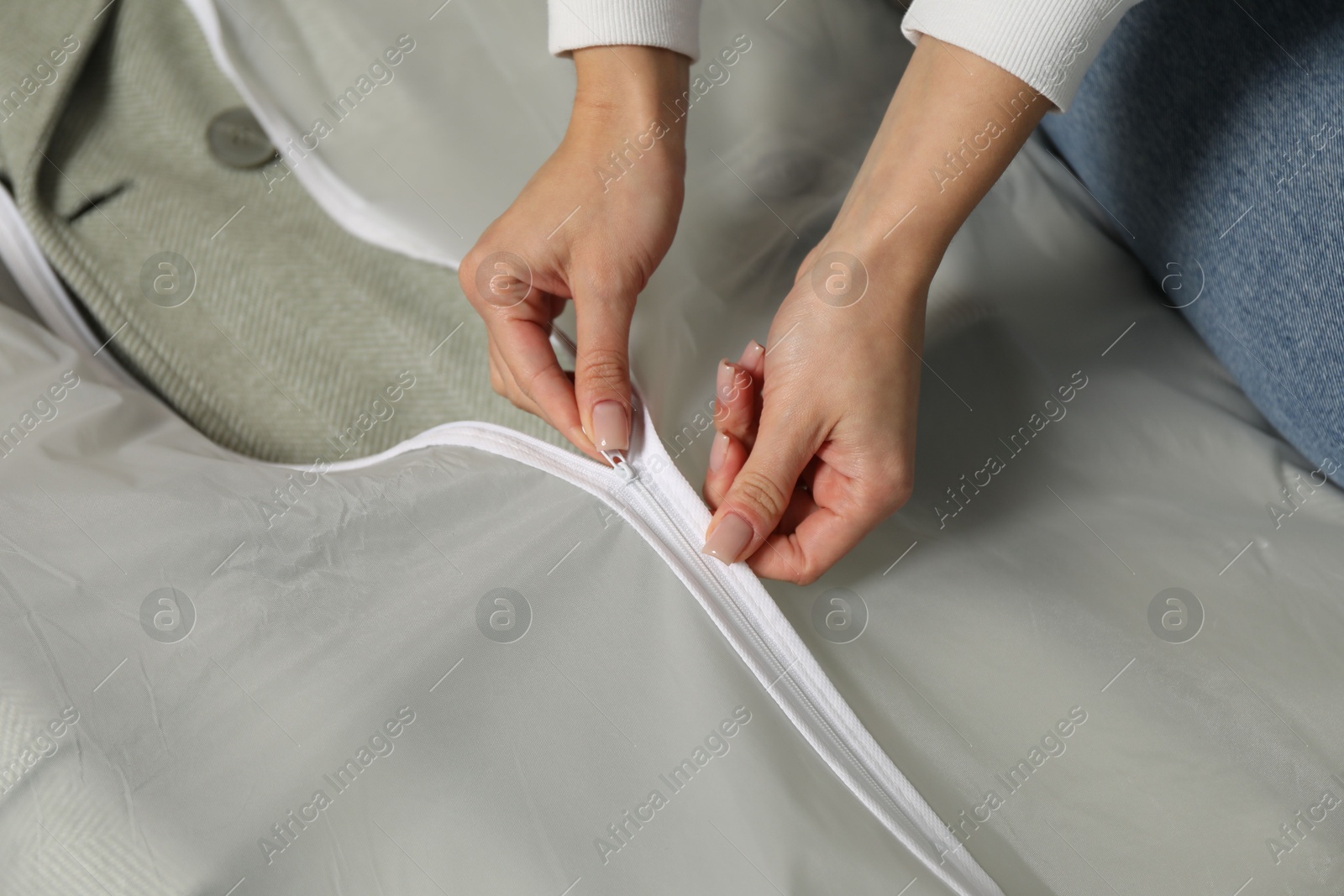 Photo of Woman zipping garment cover with clothes, closeup