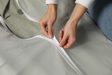 Photo of Woman zipping garment cover with clothes, closeup