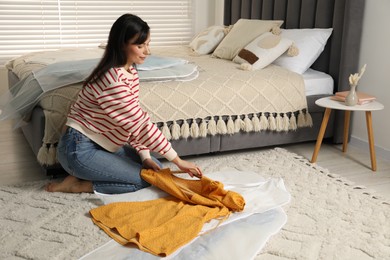 Woman putting clothes into garment cover on floor indoors