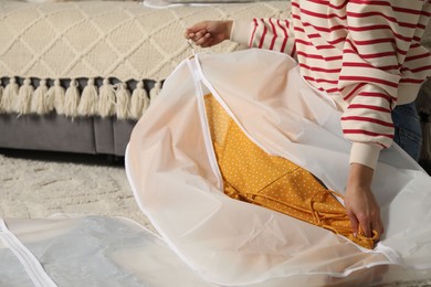 Photo of Woman putting clothes into garment cover on floor indoors, closeup