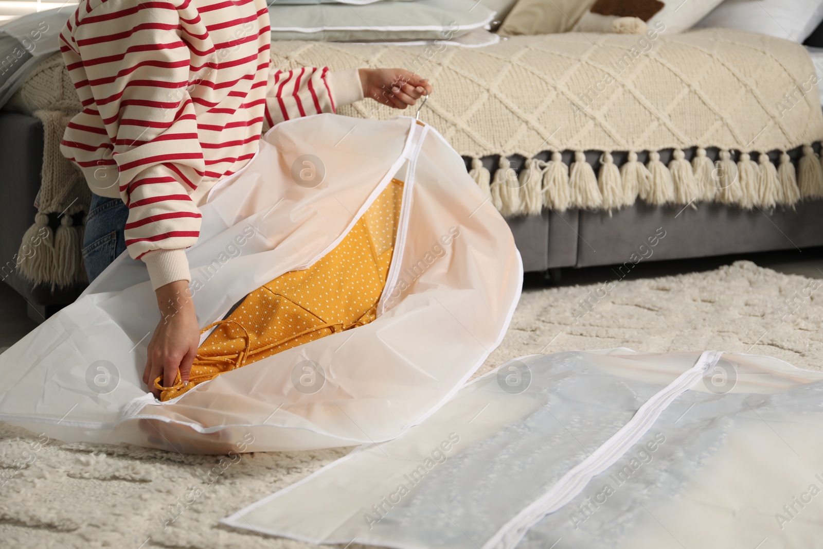 Photo of Woman putting clothes into garment cover on floor indoors, closeup