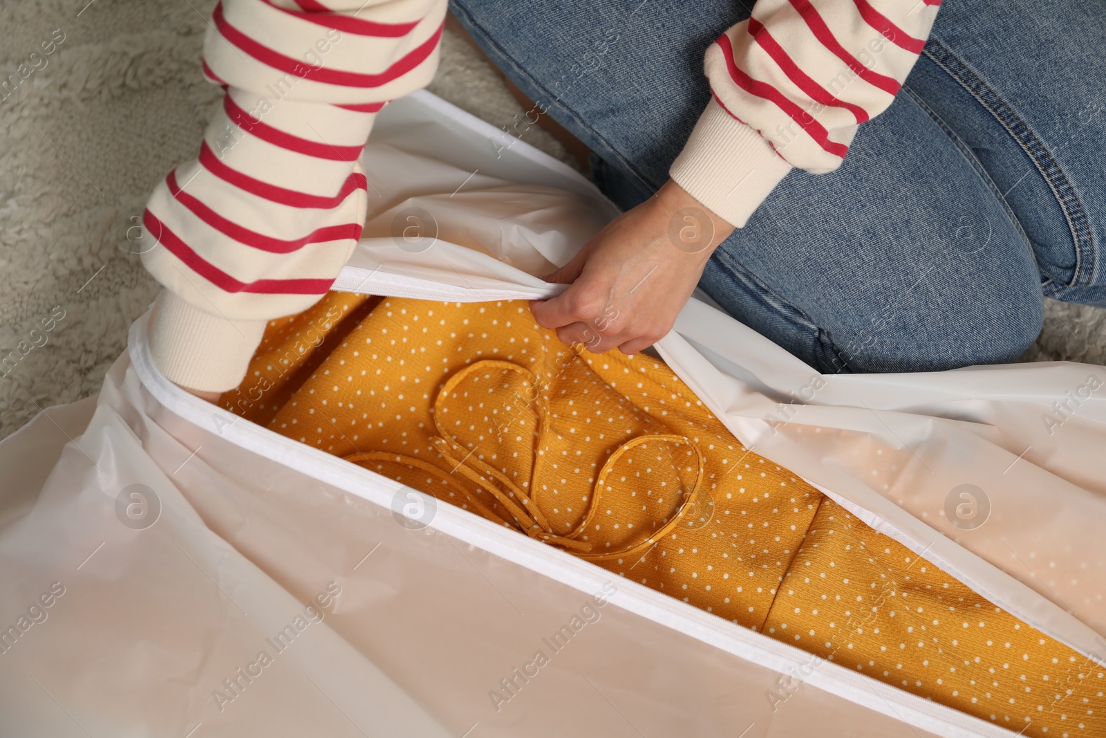 Photo of Woman putting clothes into garment cover on floor indoors, closeup