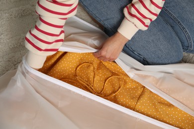 Photo of Woman putting clothes into garment cover on floor indoors, closeup