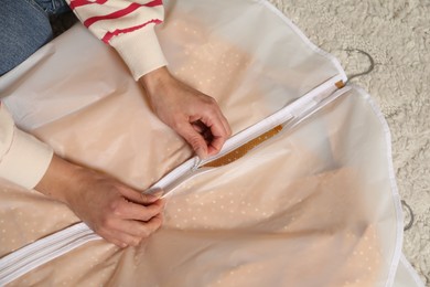 Photo of Woman zipping garment cover with clothes indoors, above view