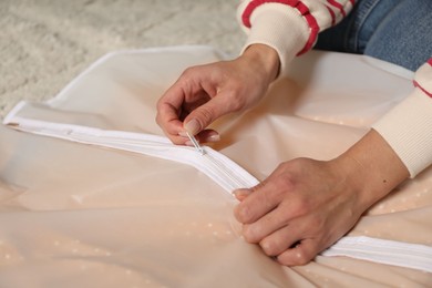 Photo of Woman zipping garment cover with clothes indoors, closeup