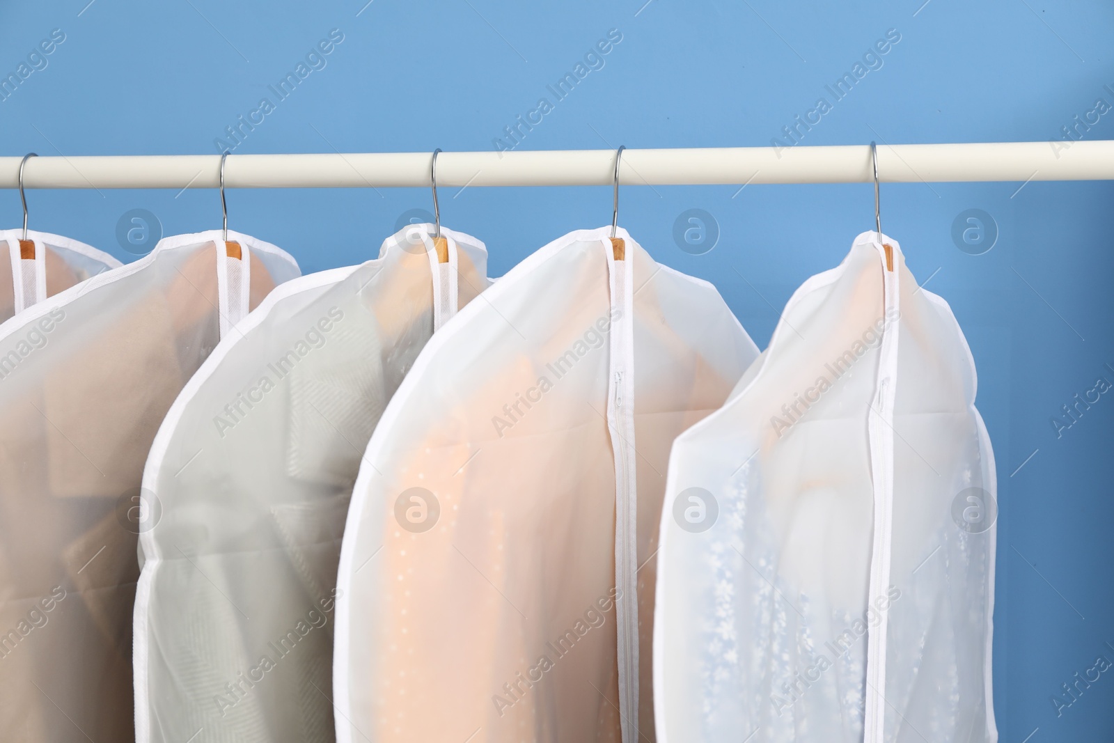 Photo of Garment covers with clothes on rack near blue wall indoors, closeup