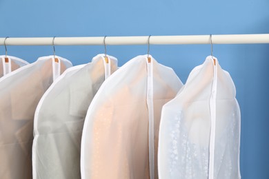 Photo of Garment covers with clothes on rack near blue wall indoors, closeup