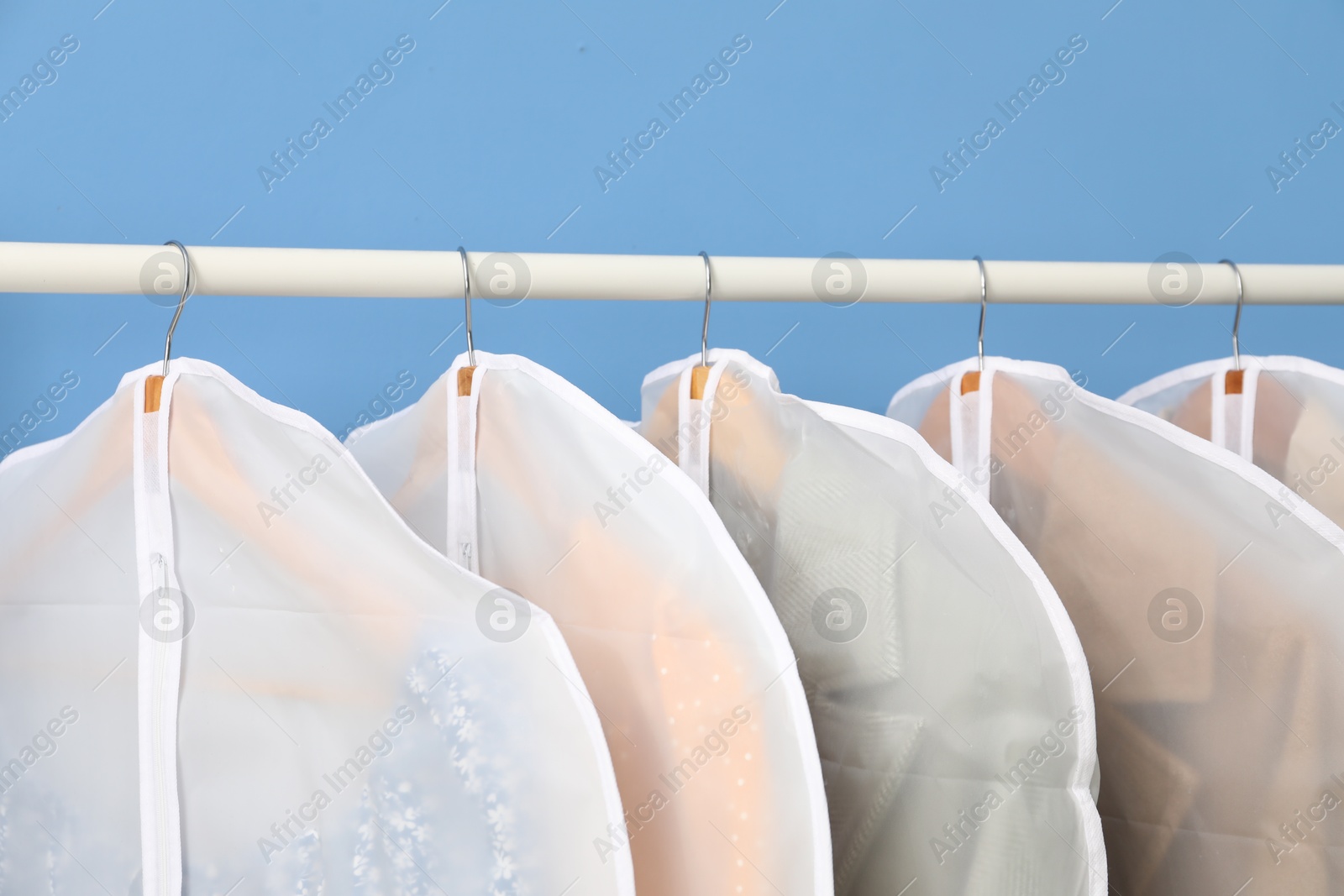 Photo of Garment covers with clothes on rack near blue wall indoors, closeup