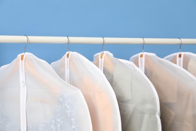 Photo of Garment covers with clothes on rack near blue wall indoors, closeup