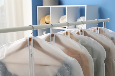 Photo of Garment covers with clothes on rack indoors, closeup