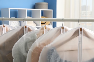 Photo of Garment covers with clothes on rack indoors, closeup