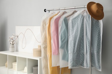 Photo of Garment covers with clothes and hat on rack near grey wall indoors