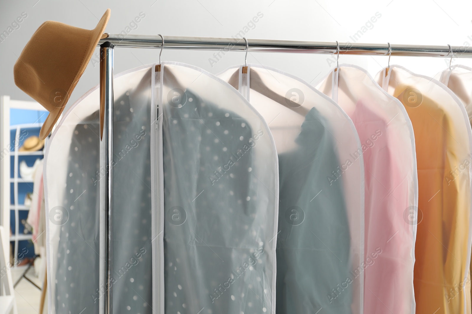 Photo of Garment covers with clothes and hat on rack indoors