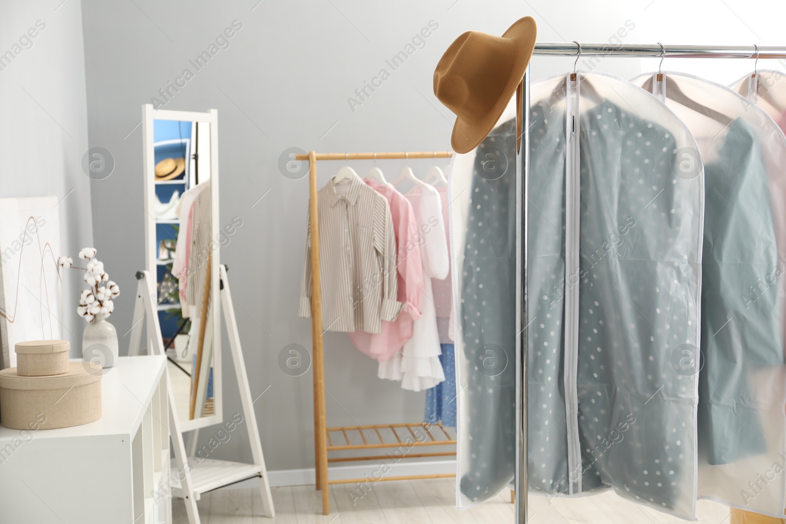 Photo of Garment covers with clothes and hat on rack indoors