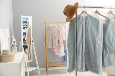 Photo of Garment covers with clothes and hat on rack indoors