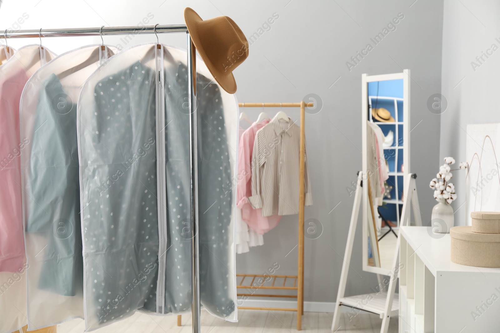 Photo of Garment covers with clothes and hat on rack indoors