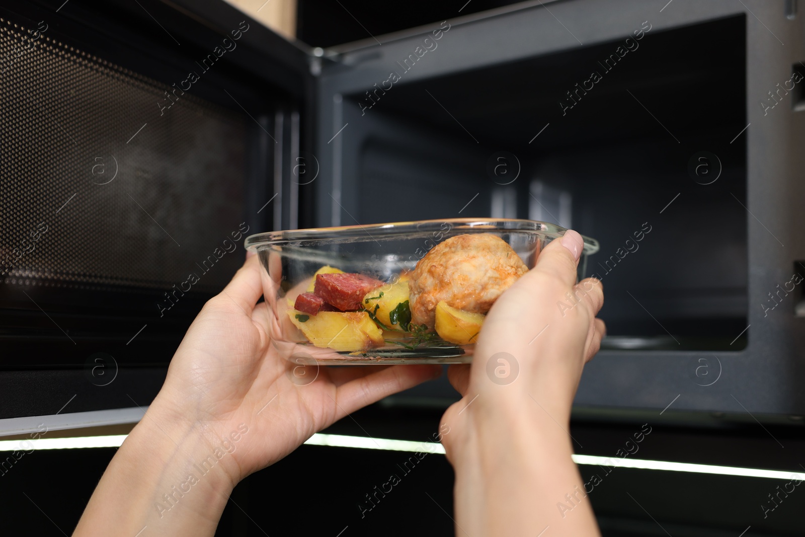 Photo of Woman putting container with lunch into microwave indoors, closeup