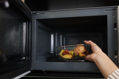 Photo of Woman putting container with lunch into microwave indoors, closeup