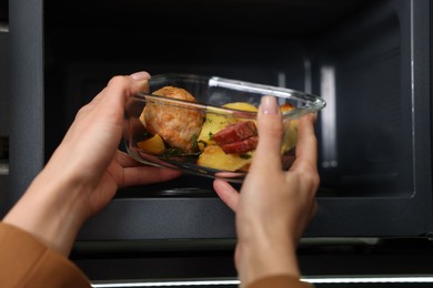 Photo of Woman putting container with lunch into microwave indoors, closeup