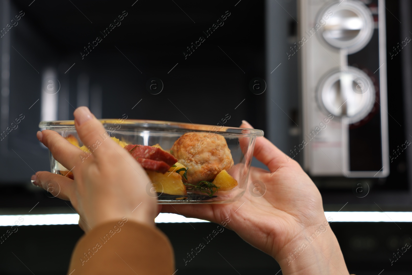 Photo of Woman putting container with lunch into microwave indoors, closeup