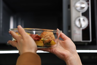 Photo of Woman putting container with lunch into microwave indoors, closeup