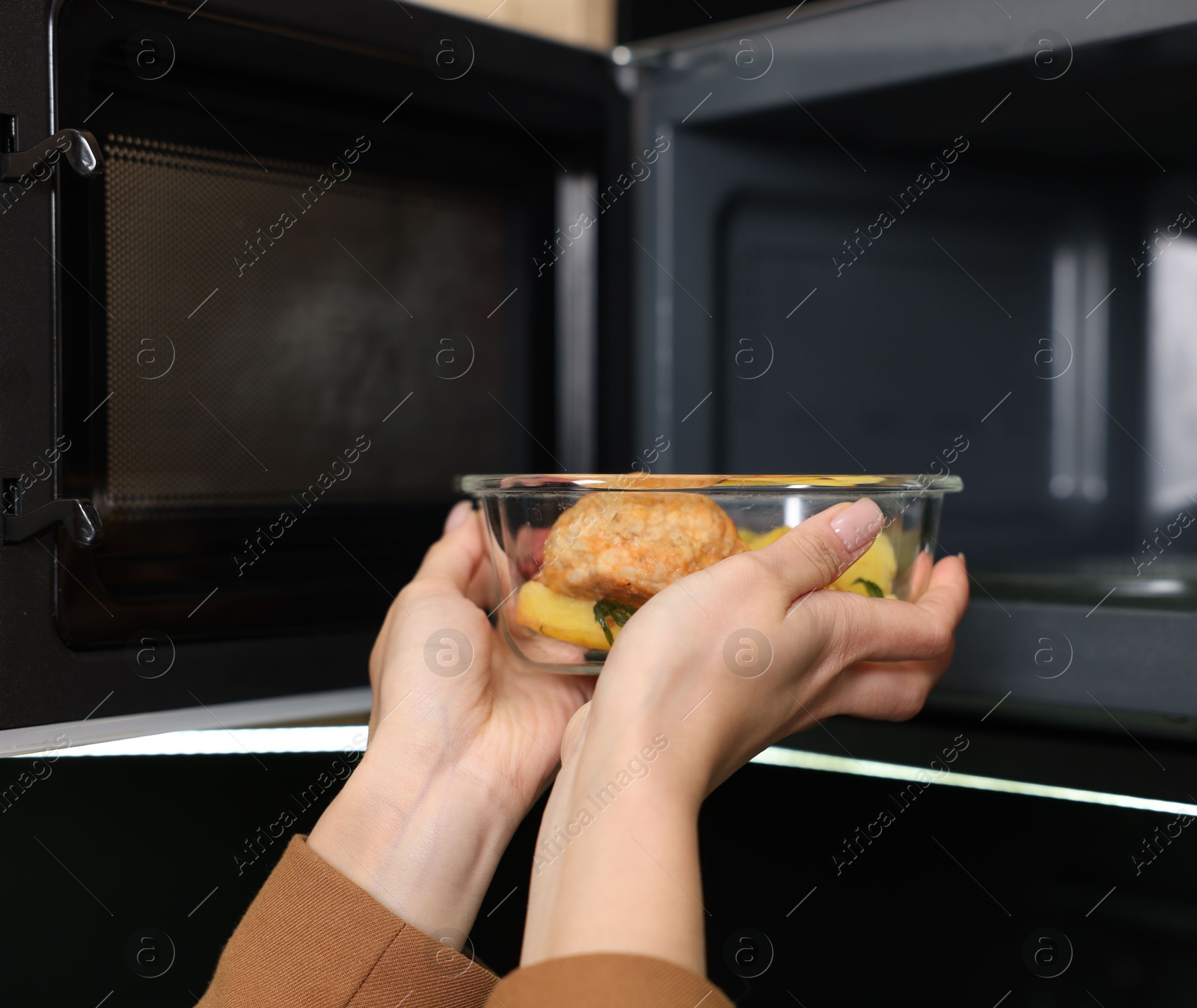 Photo of Woman putting container with lunch into microwave indoors, closeup