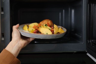 Photo of Woman putting plate with lunch into microwave indoors, closeup