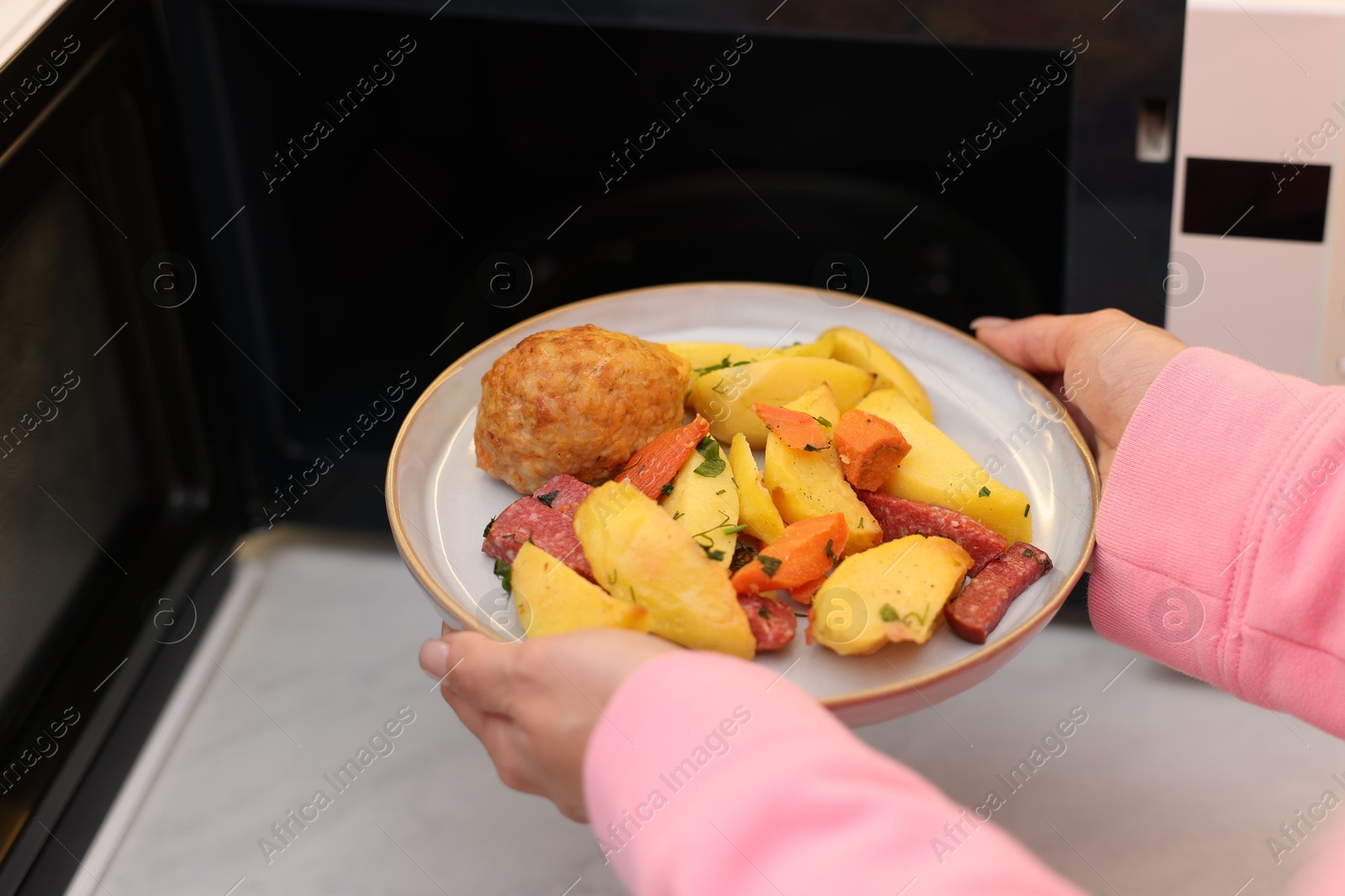 Photo of Woman putting plate with lunch into microwave indoors, closeup