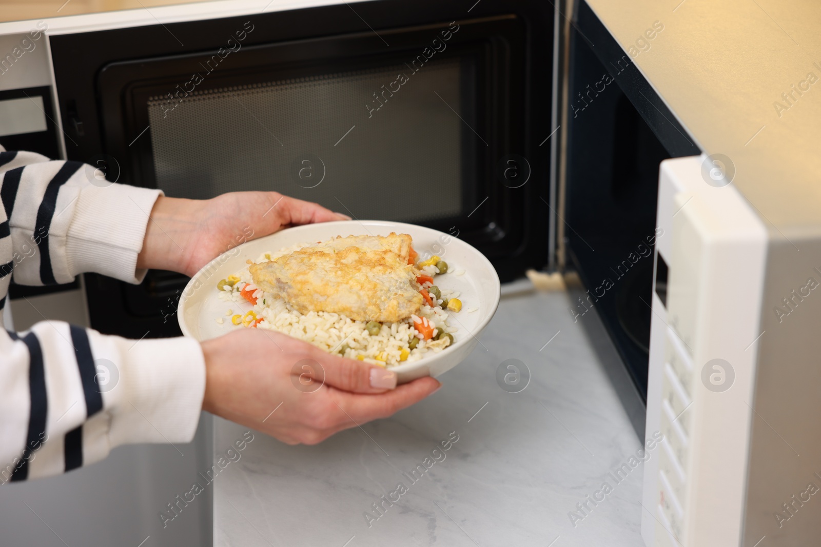 Photo of Woman putting plate with lunch into microwave indoors, closeup