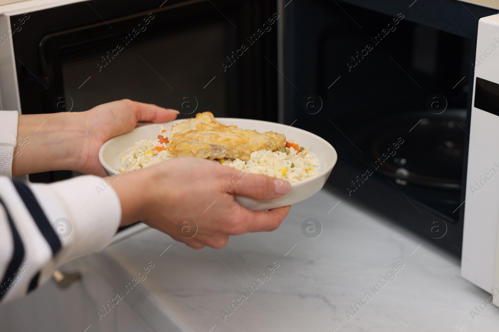 Photo of Woman putting plate with lunch into microwave indoors, closeup