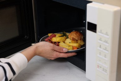 Photo of Woman putting plate with lunch into microwave indoors, closeup