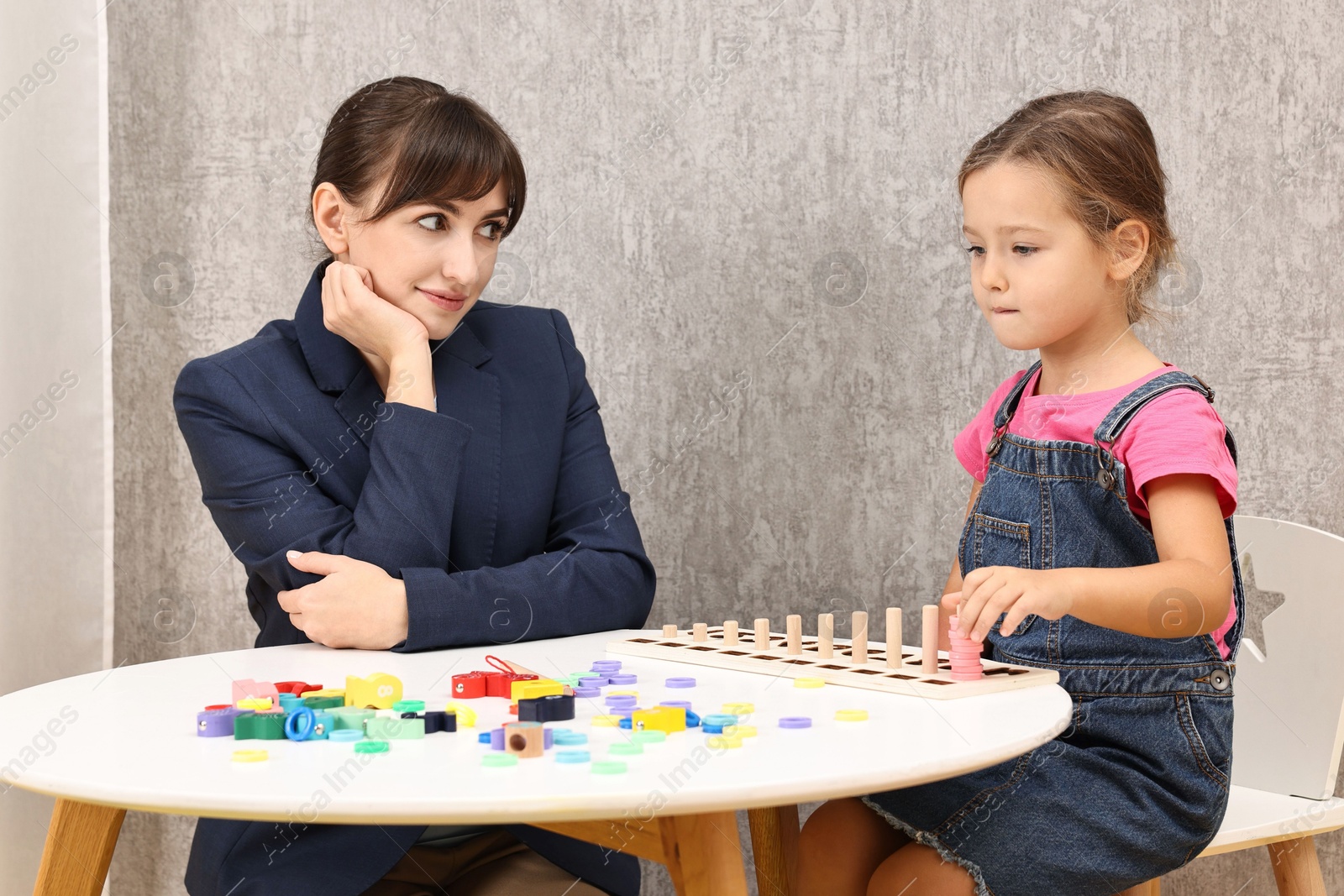 Photo of Autism therapy. Psychologist and little girl playing with educational toy at table in mental health center