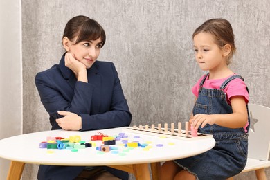 Photo of Autism therapy. Psychologist and little girl playing with educational toy at table in mental health center